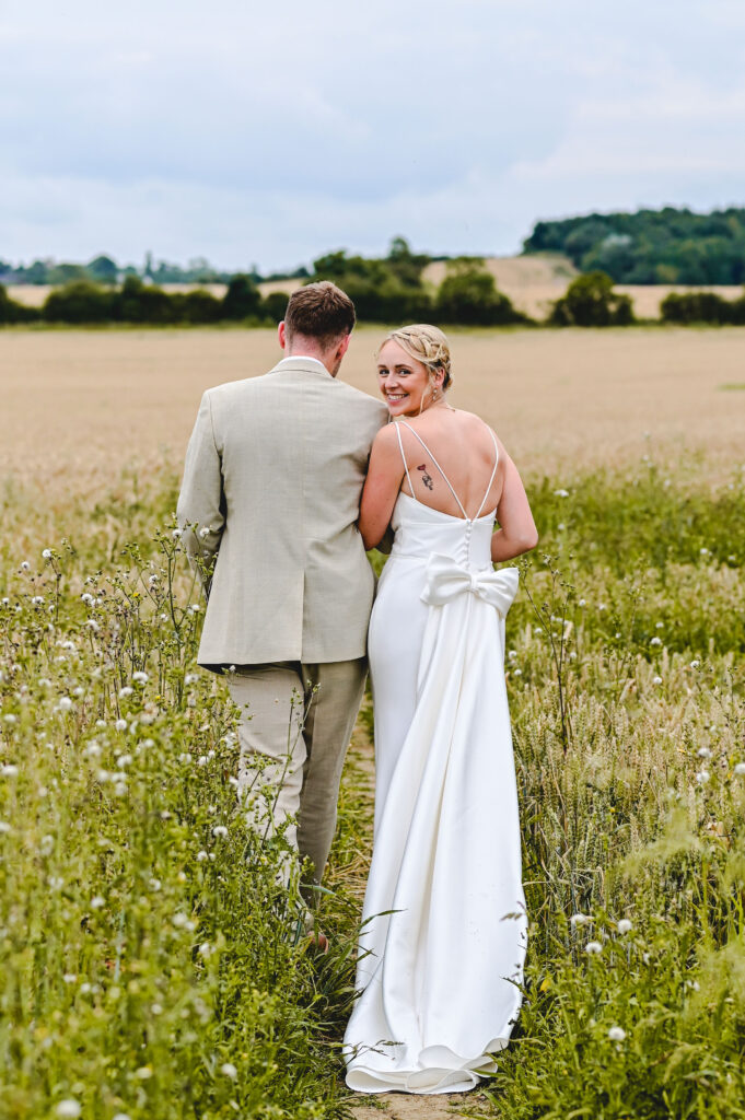 A bridal couple walking through a field with the bride looking back, captured by Josie Parr Leicestershire based wedding photographer